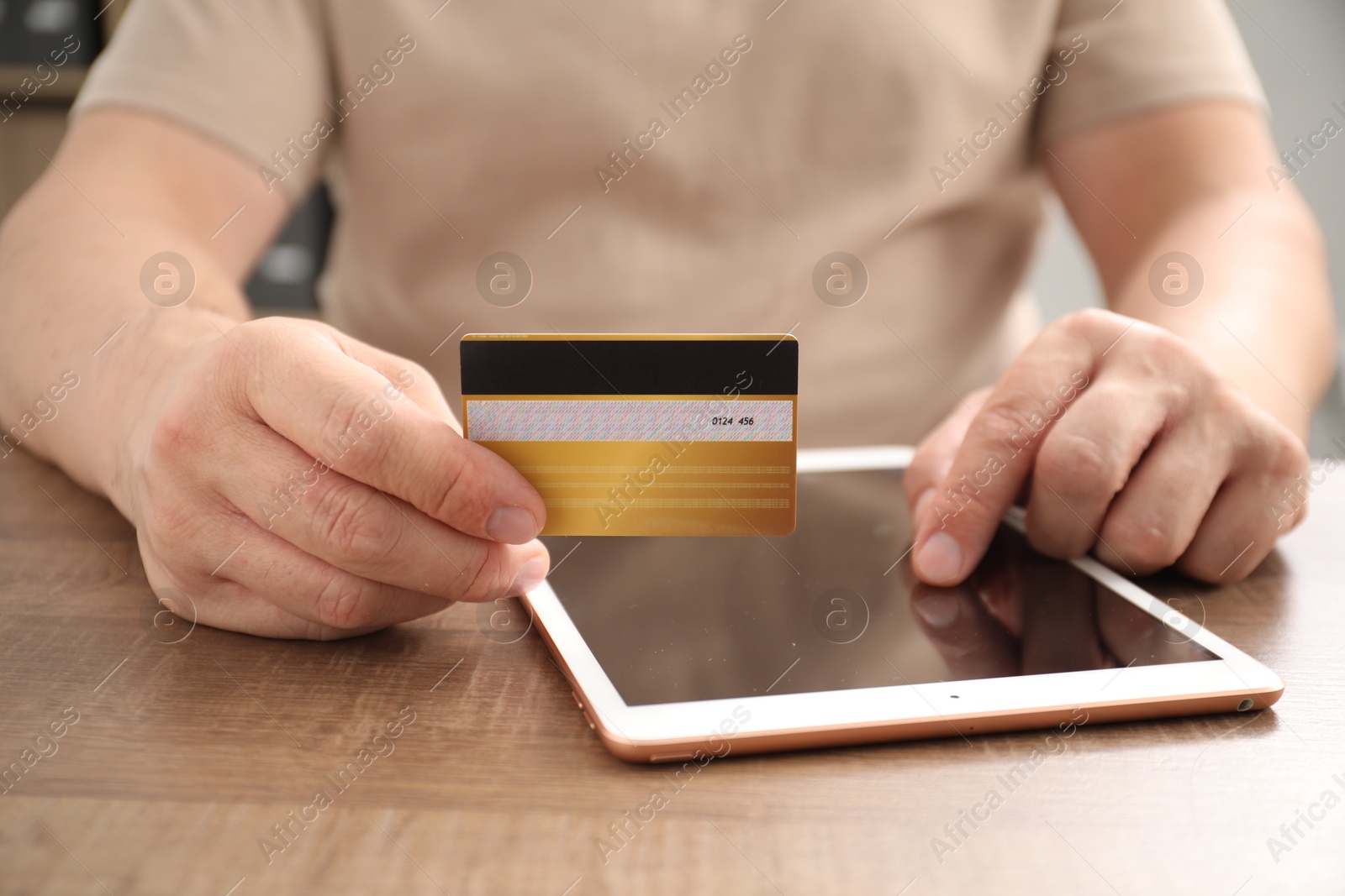 Photo of Man with credit card using tablet at wooden table indoors, closeup