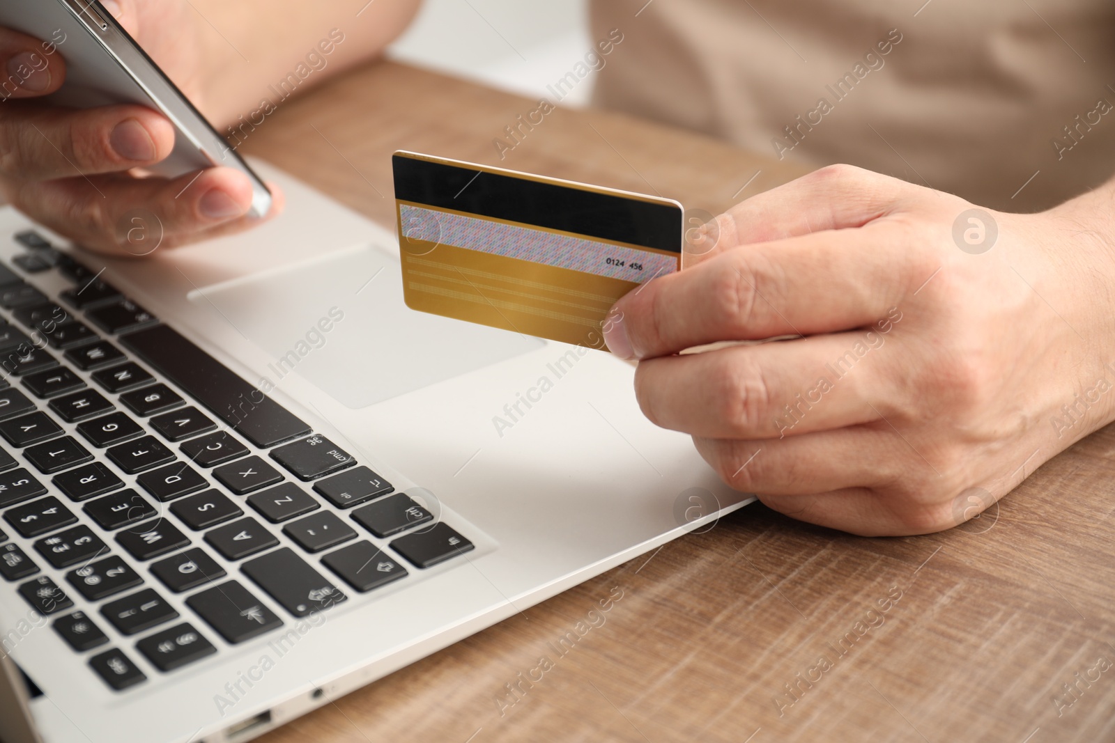 Photo of Man with credit card and smartphone at wooden table indoors, closeup