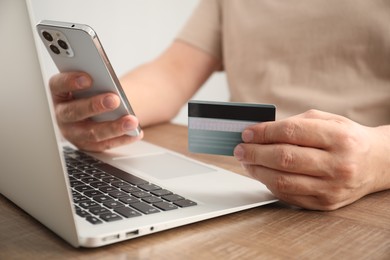 Photo of Man with credit card and smartphone at wooden table indoors, closeup