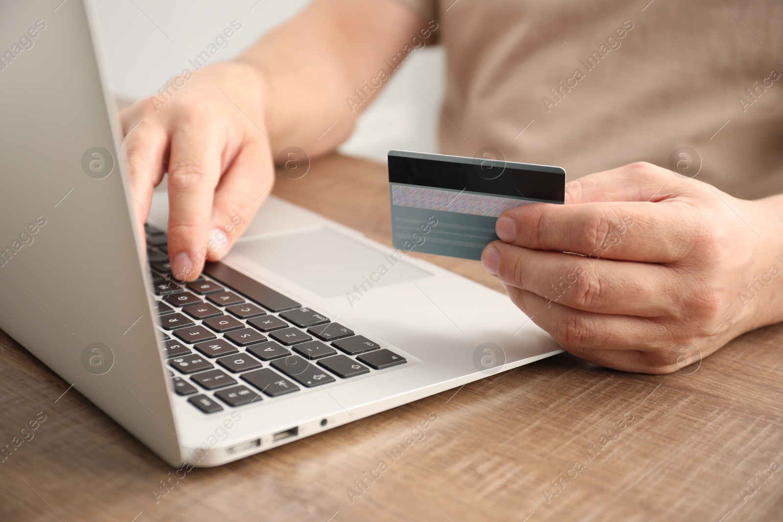 Photo of Man with credit card using laptop at wooden table indoors, closeup