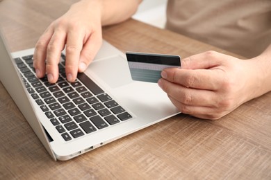 Photo of Man with credit card using laptop at wooden table, closeup