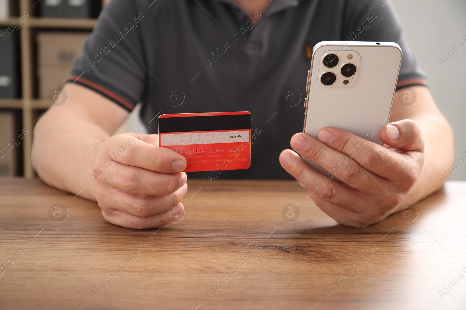 Photo of Man with credit card and smartphone at wooden table indoors, closeup