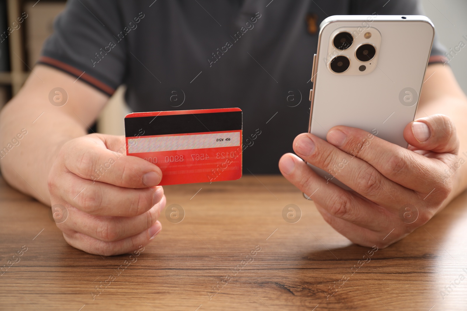 Photo of Man with credit card and smartphone at wooden table indoors, closeup