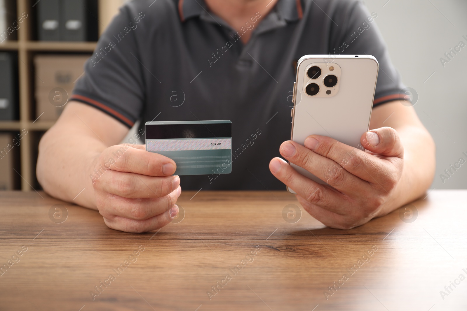 Photo of Man with credit card and smartphone at wooden table indoors, closeup