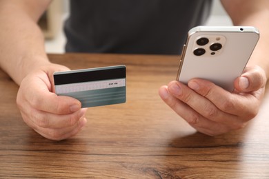 Photo of Man with credit card and smartphone at wooden table indoors, closeup