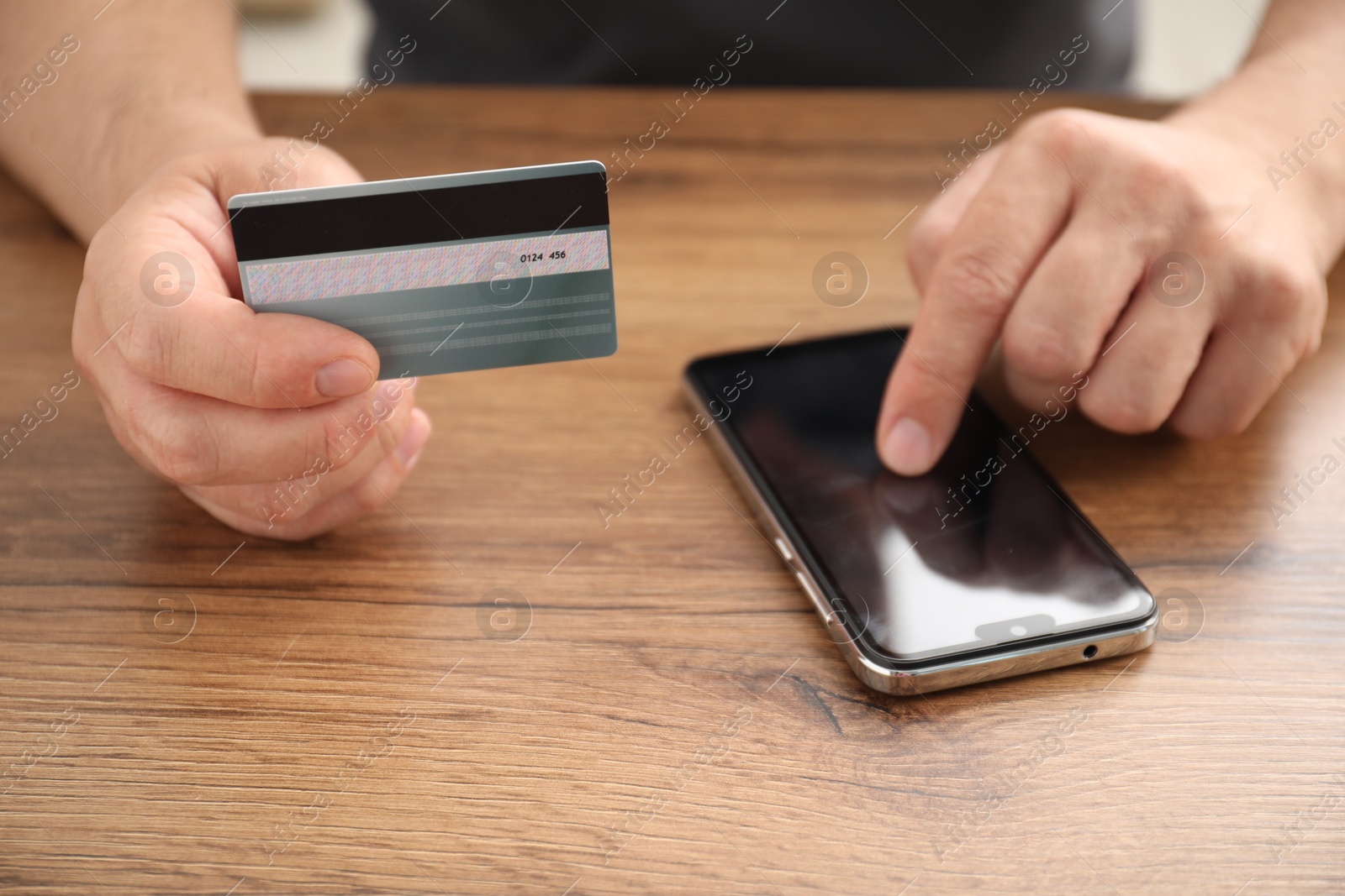 Photo of Man with credit card using smartphone at wooden table indoors, closeup