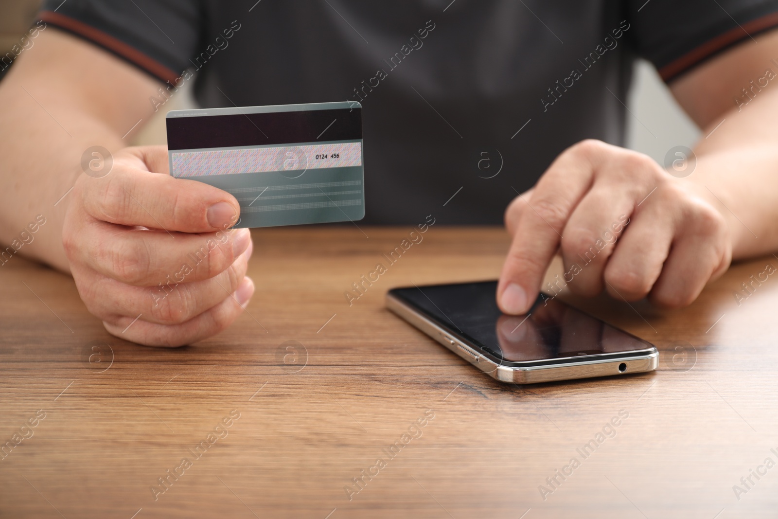 Photo of Man with credit card using smartphone at wooden table indoors, closeup