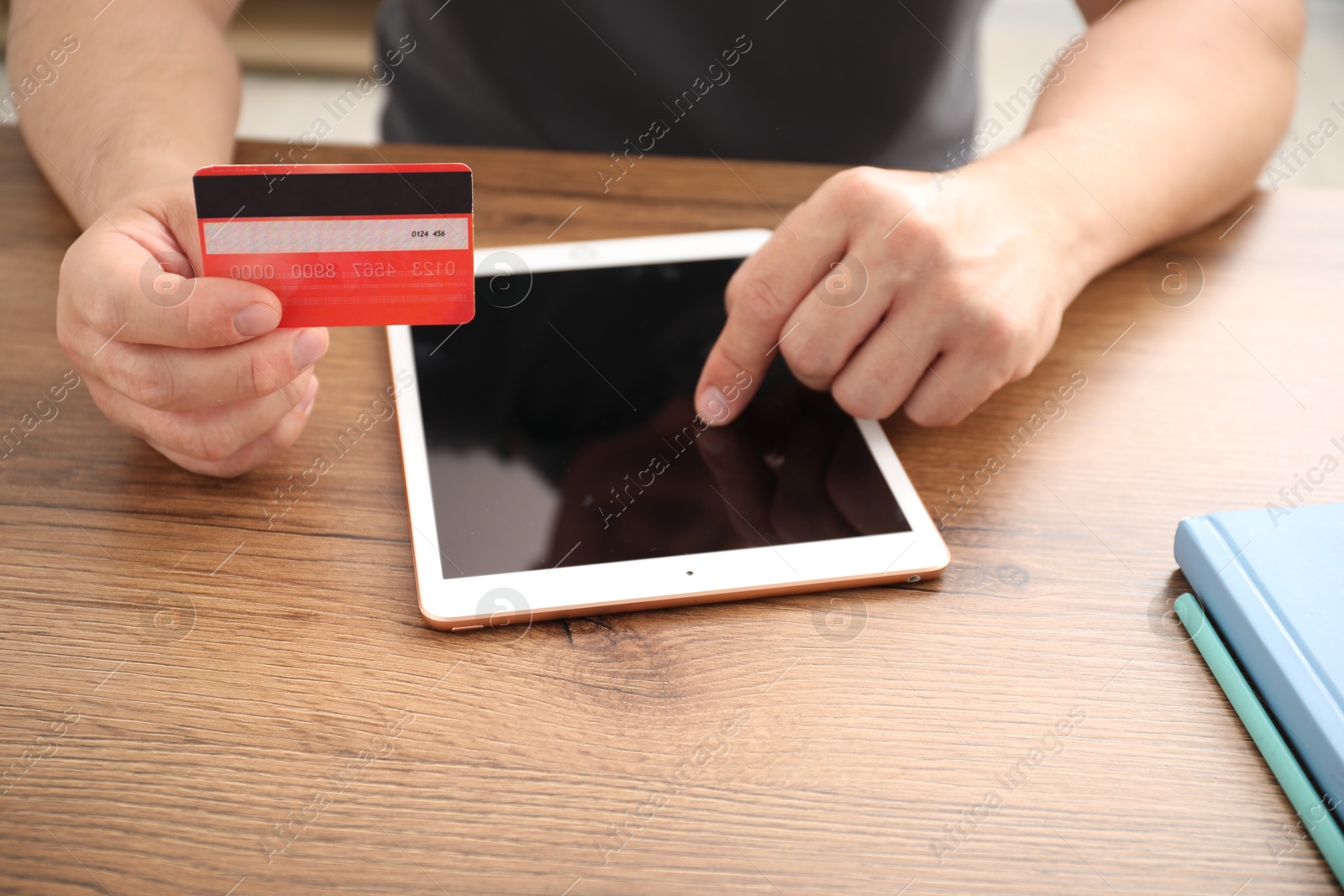 Photo of Man with credit card using tablet at wooden table indoors, closeup