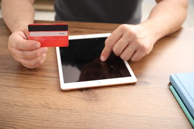 Photo of Man with credit card using tablet at wooden table indoors, closeup