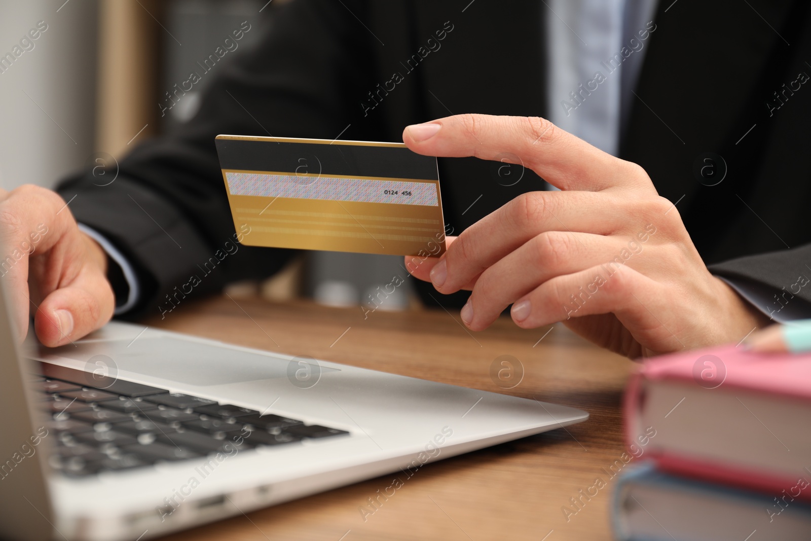 Photo of Man with credit card using laptop at wooden table indoors, closeup