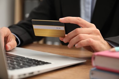 Photo of Man with credit card using laptop at wooden table indoors, closeup