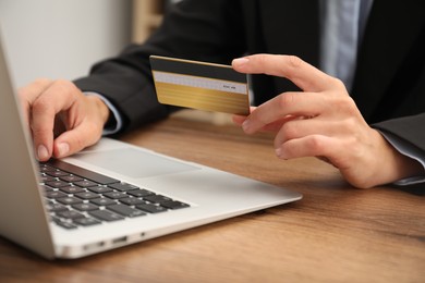 Photo of Man with credit card using laptop at wooden table indoors, closeup