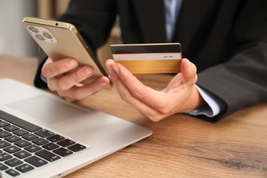 Photo of Man with credit card and smartphone at wooden table indoors, closeup