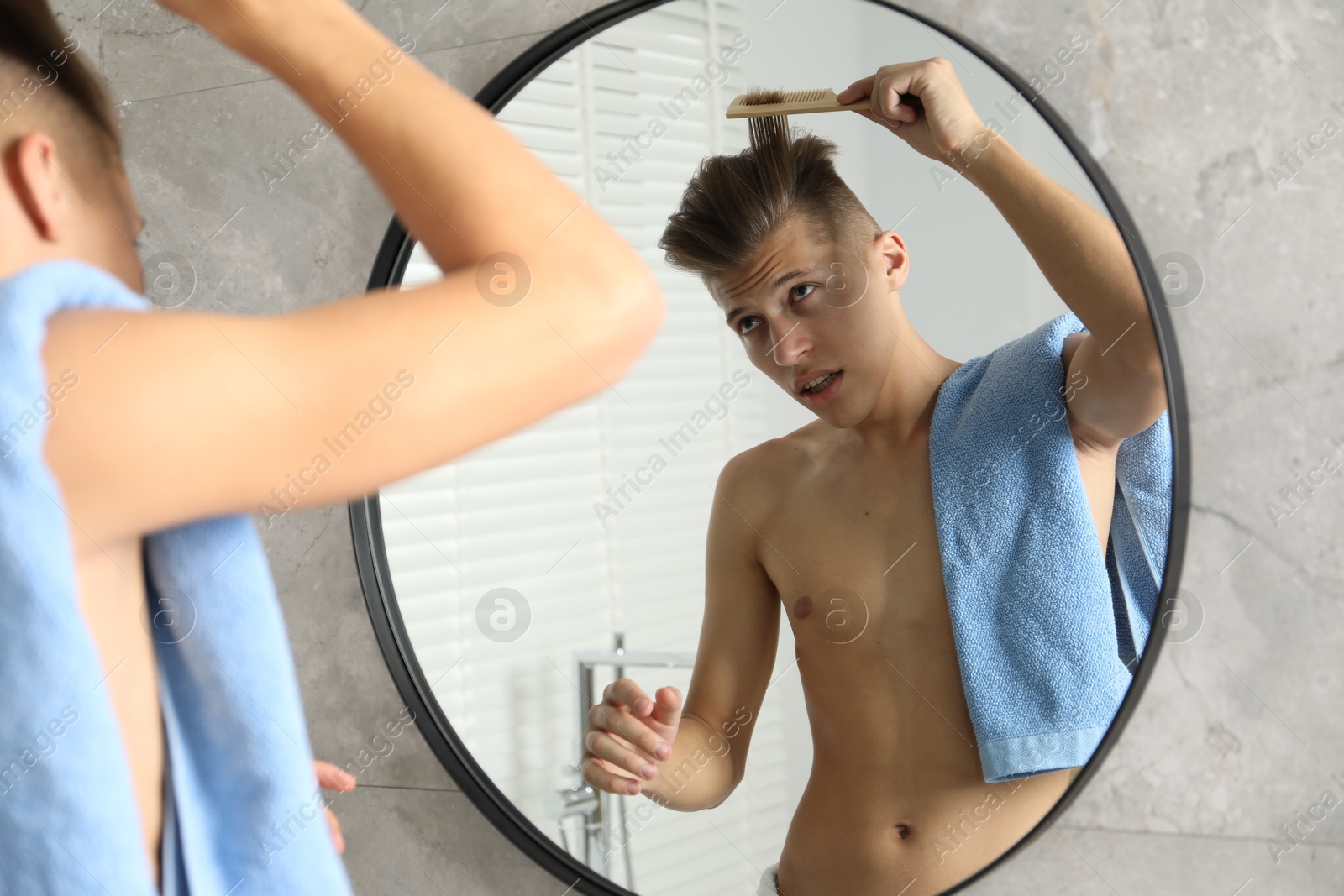 Photo of Handsome man brushing his hair near mirror in bathroom