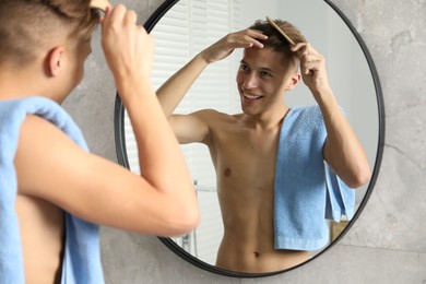 Photo of Handsome man brushing his hair near mirror in bathroom