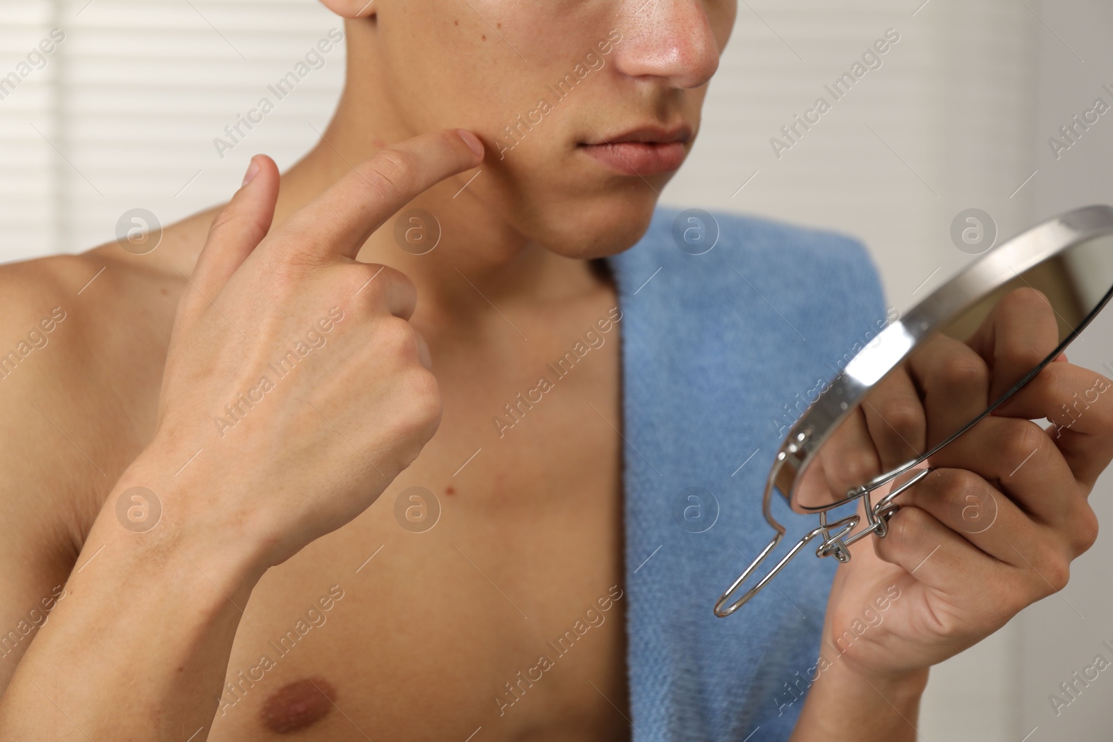 Photo of Man with mirror touching his face in bathroom, closeup