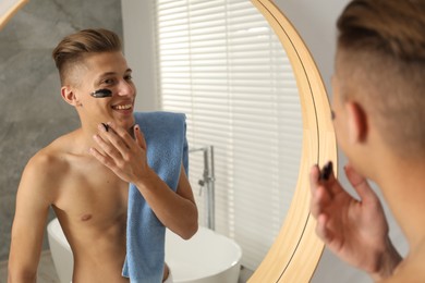 Photo of Handsome man applying mask onto his face near mirror in bathroom