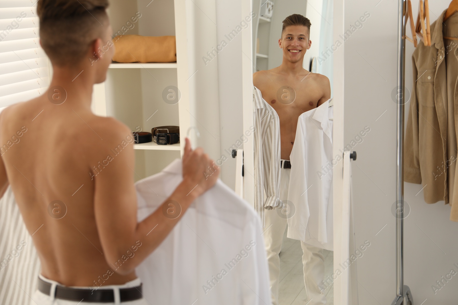 Photo of Handsome man choosing clothes near mirror indoors