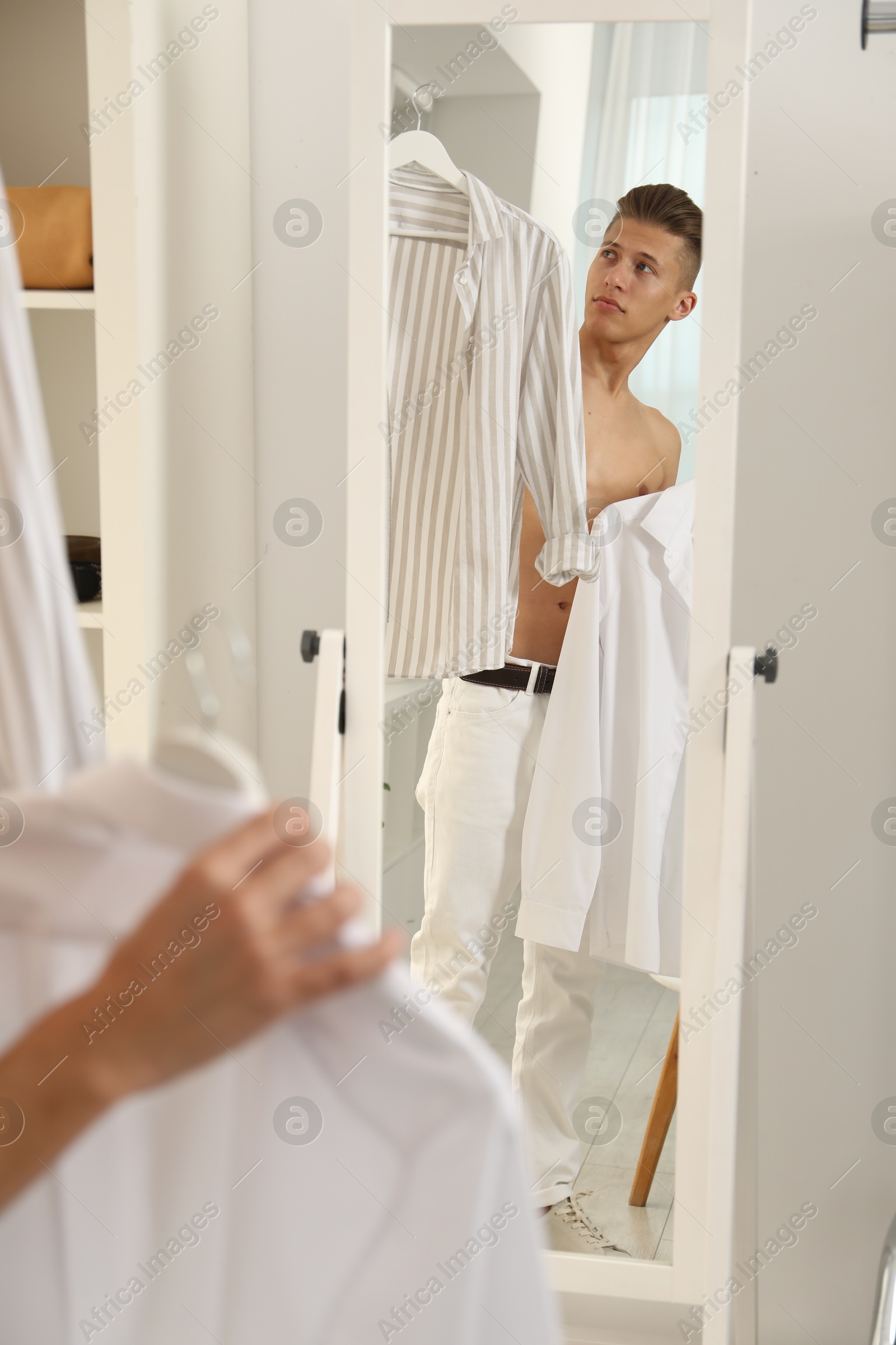 Photo of Handsome man choosing clothes near mirror indoors