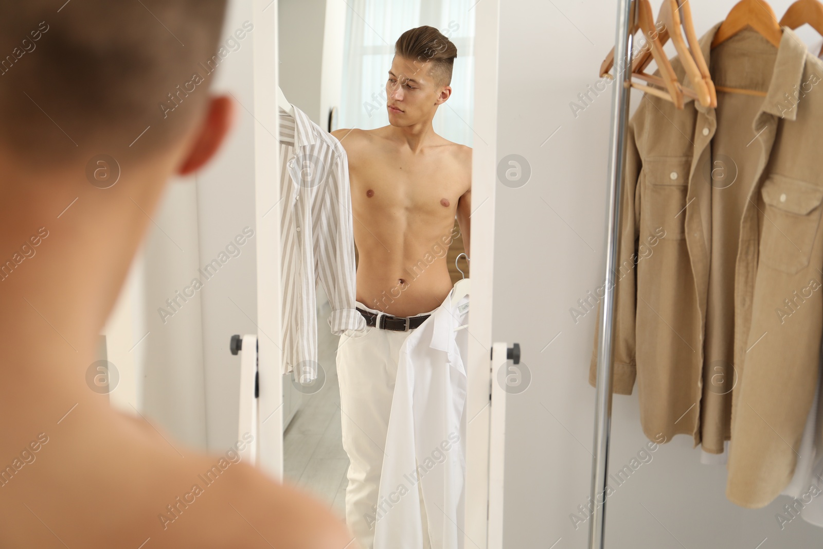 Photo of Handsome man choosing clothes near mirror indoors