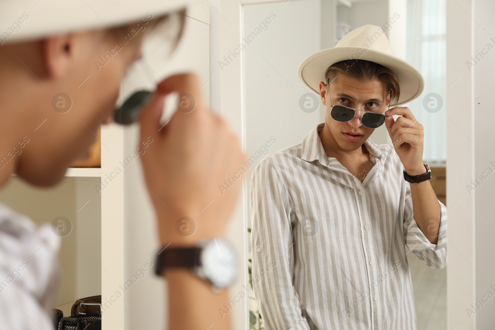 Photo of Handsome man in hat and glasses looking at mirror indoors