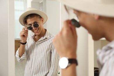 Photo of Handsome man in hat and glasses looking at mirror indoors