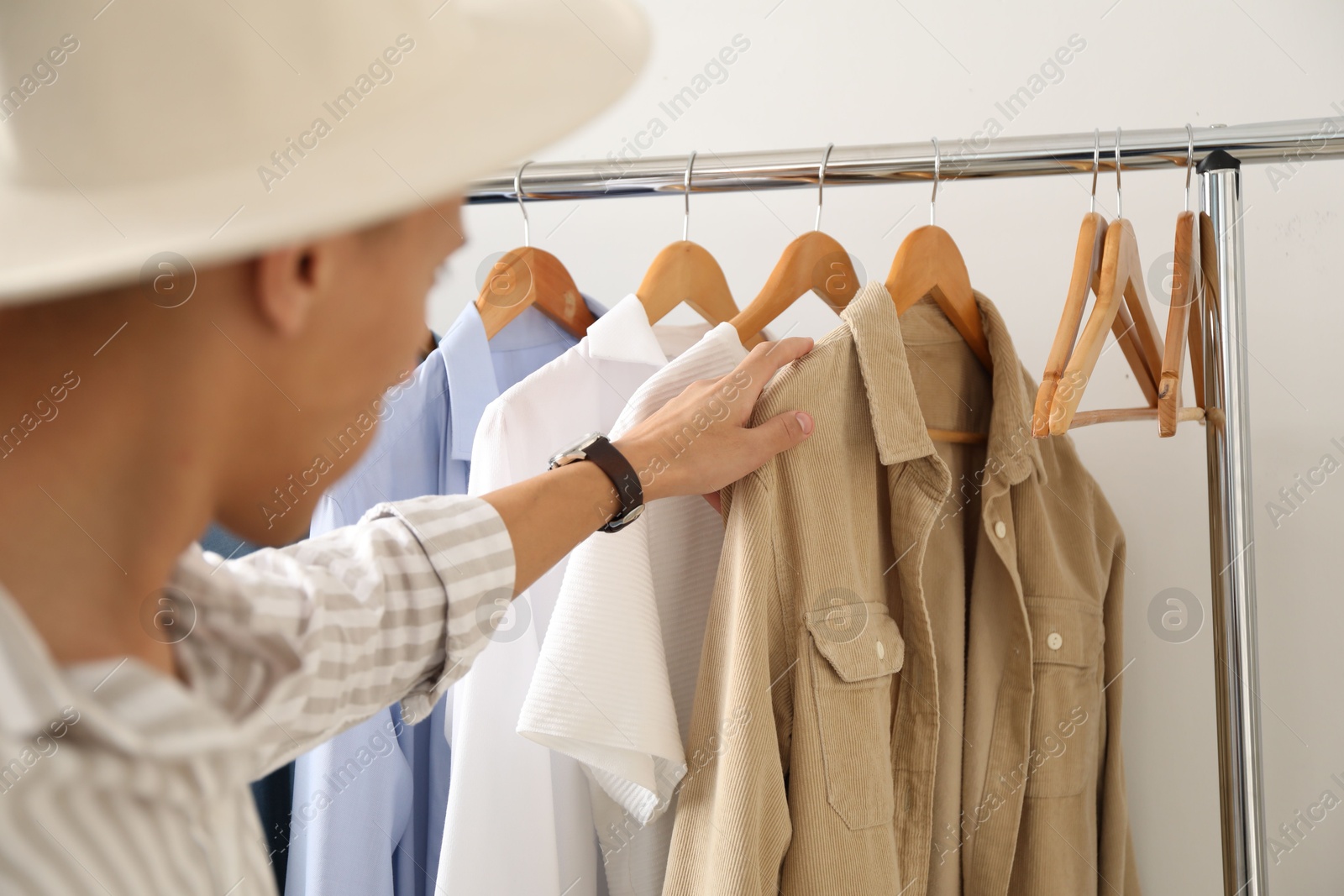 Photo of Man in hat choosing clothes near rack indoors