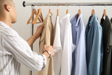 Photo of Man in shirt choosing clothes near rack indoors