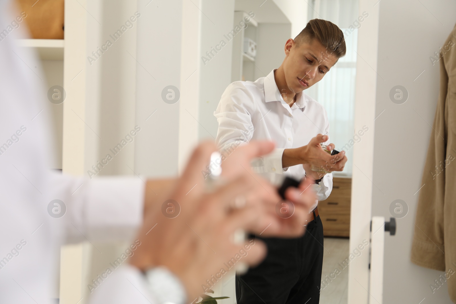 Photo of Man spraying luxury perfume near mirror indoors