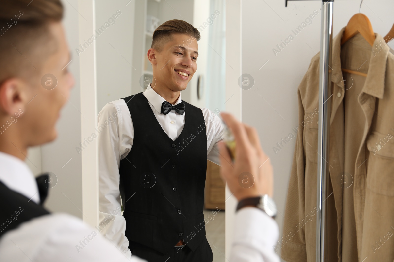 Photo of Man spraying luxury perfume near mirror indoors