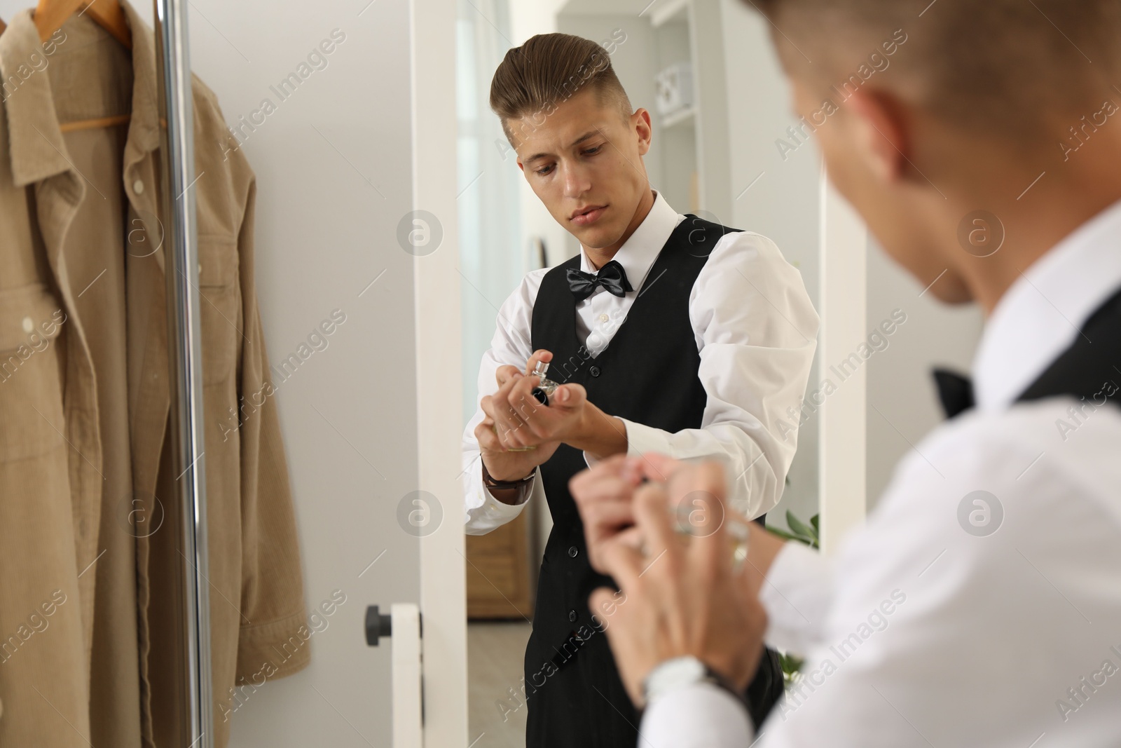 Photo of Man spraying luxury perfume near mirror indoors