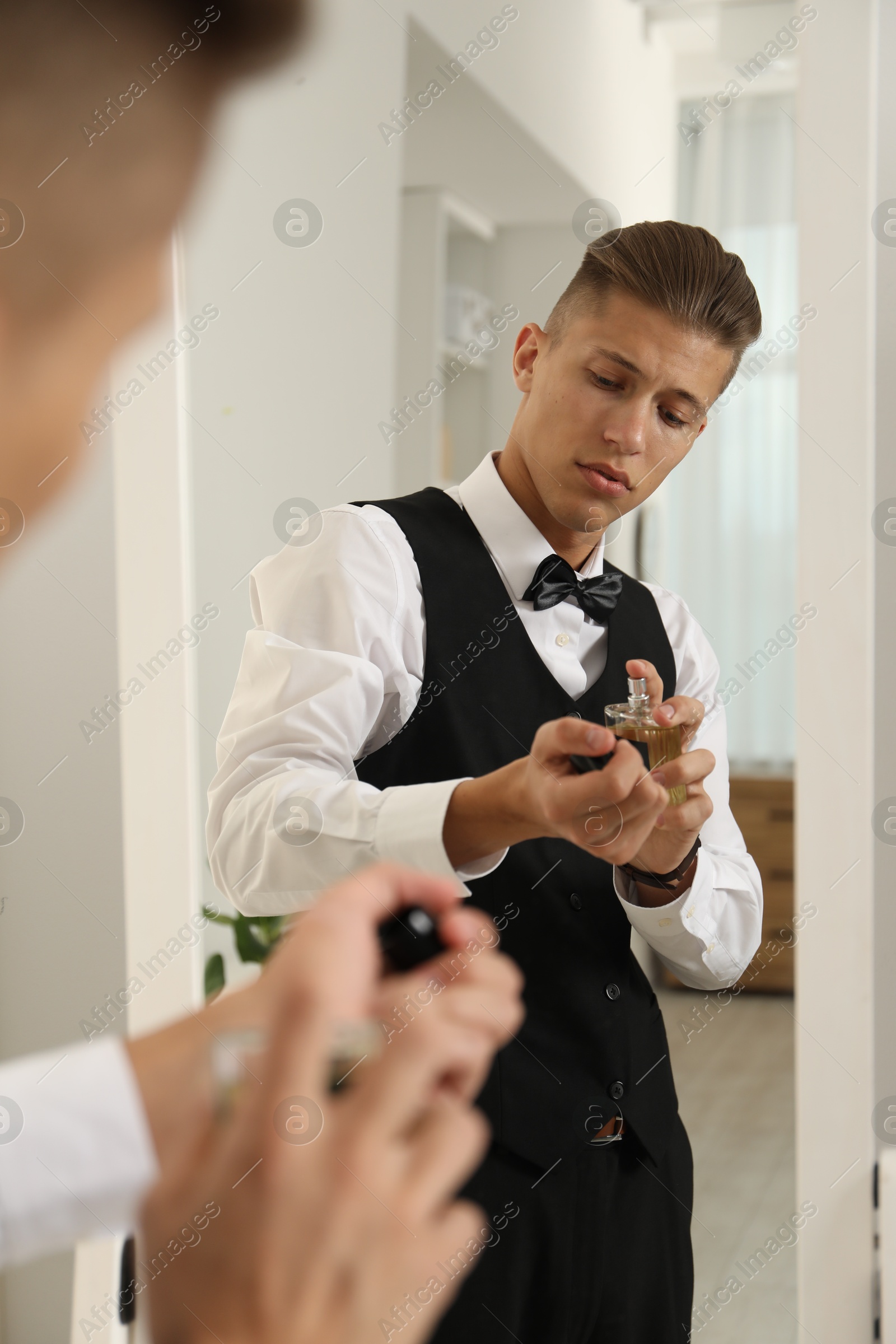 Photo of Man spraying luxury perfume near mirror indoors