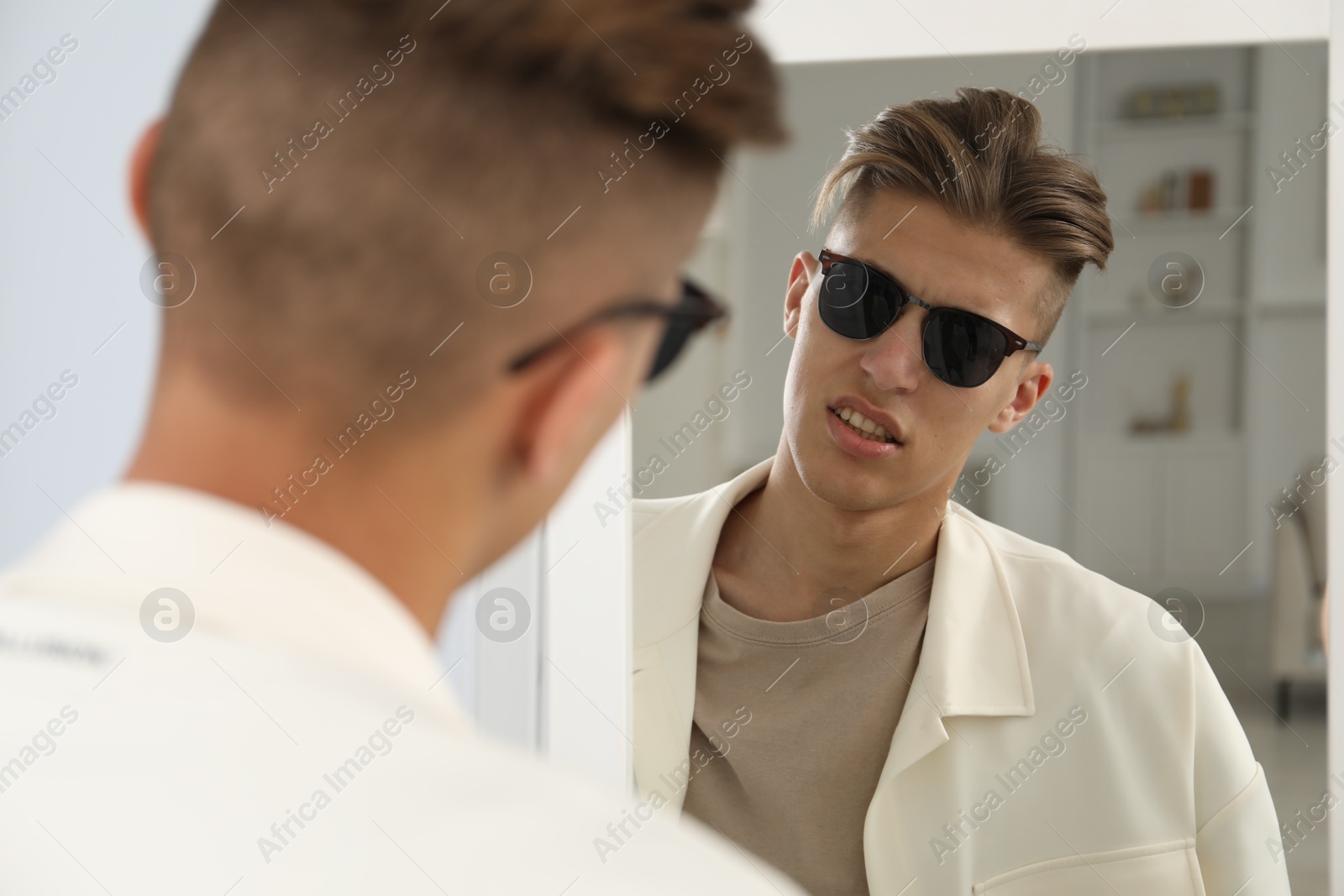 Photo of Handsome man in glasses looking at mirror indoors