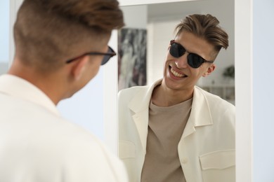 Photo of Handsome man in glasses looking at mirror indoors
