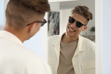 Handsome man in glasses looking at mirror indoors