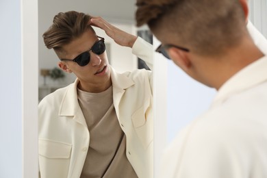 Handsome man in glasses looking at mirror indoors