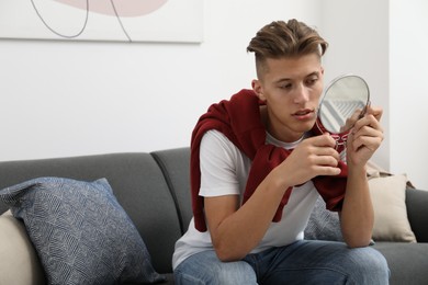 Handsome man looking at mirror on sofa at home