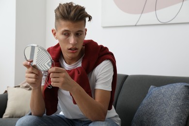 Photo of Handsome man looking at mirror on sofa at home