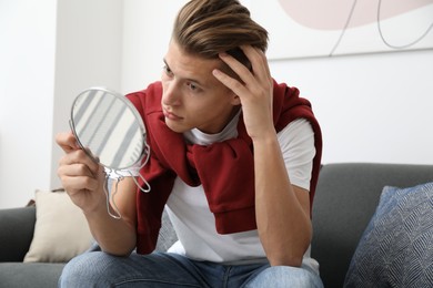 Handsome man looking at mirror on sofa at home