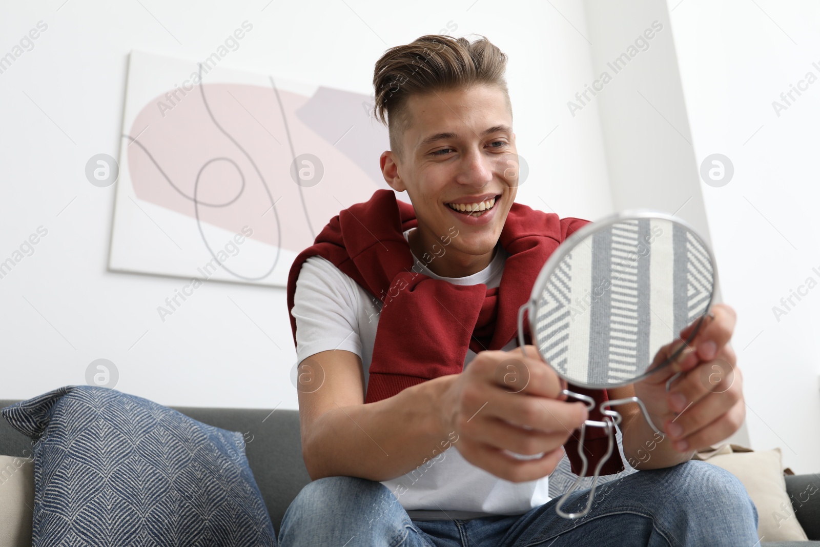 Photo of Handsome man looking at mirror on sofa at home, low angle view