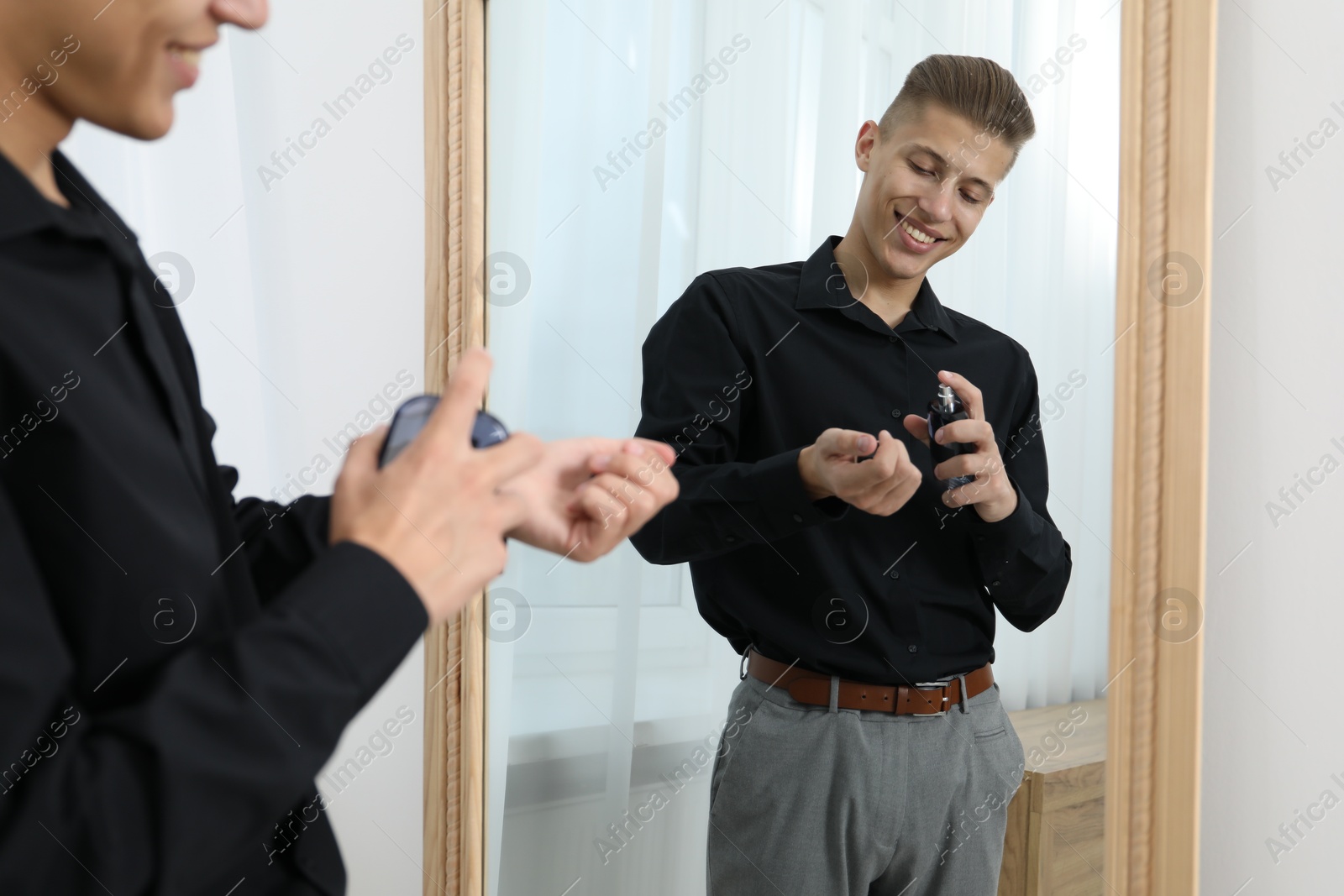 Photo of Man spraying luxury perfume near mirror indoors