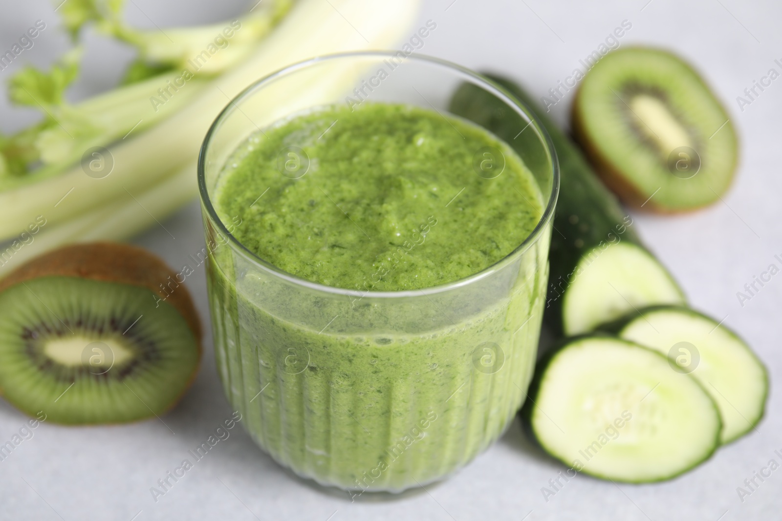 Photo of Delicious green smoothie and ingredients on light table, closeup