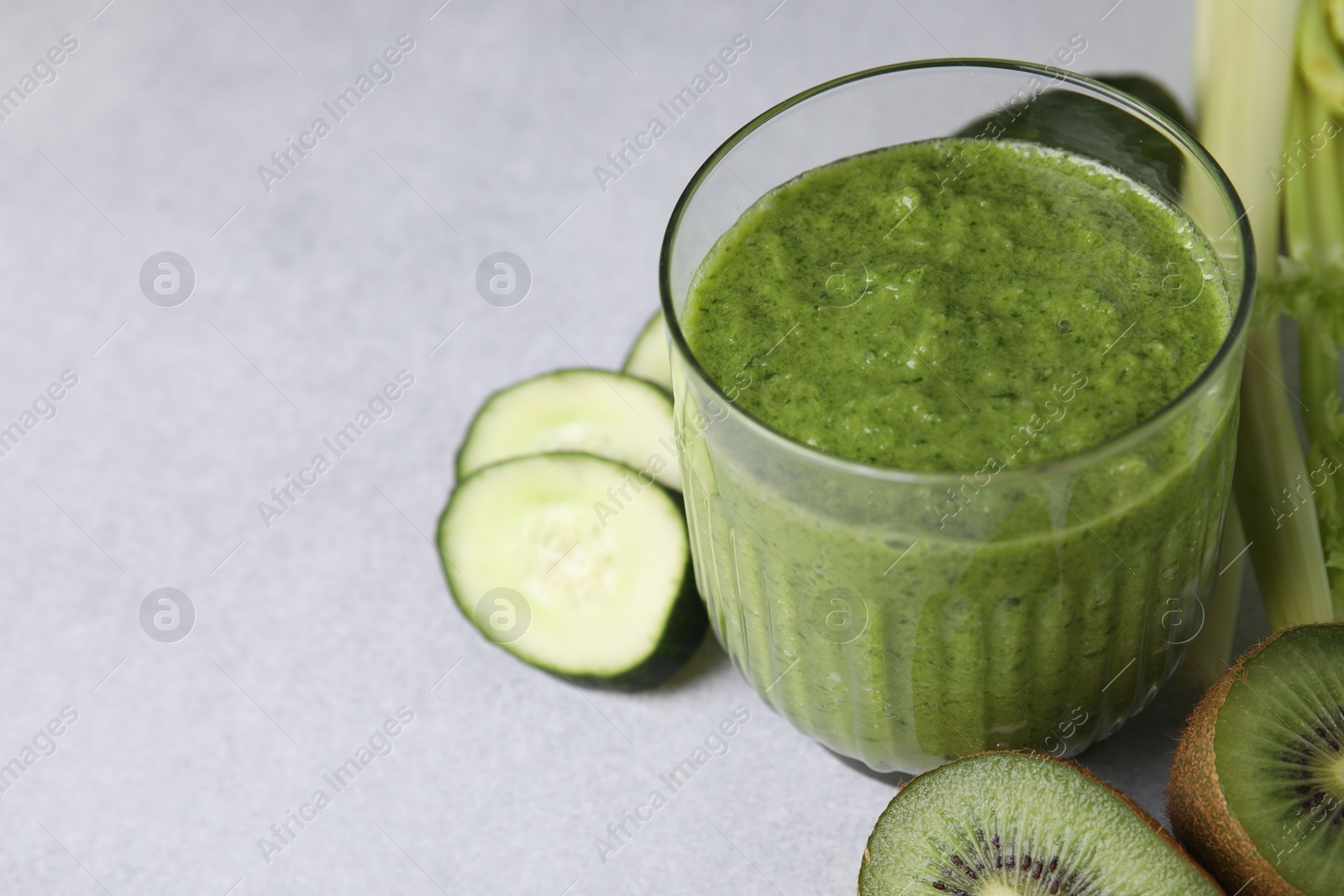 Photo of Delicious green smoothie and ingredients on light table, closeup. Space for text