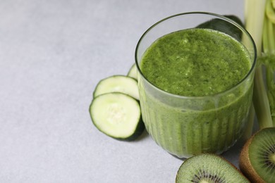 Photo of Delicious green smoothie and ingredients on light table, closeup. Space for text