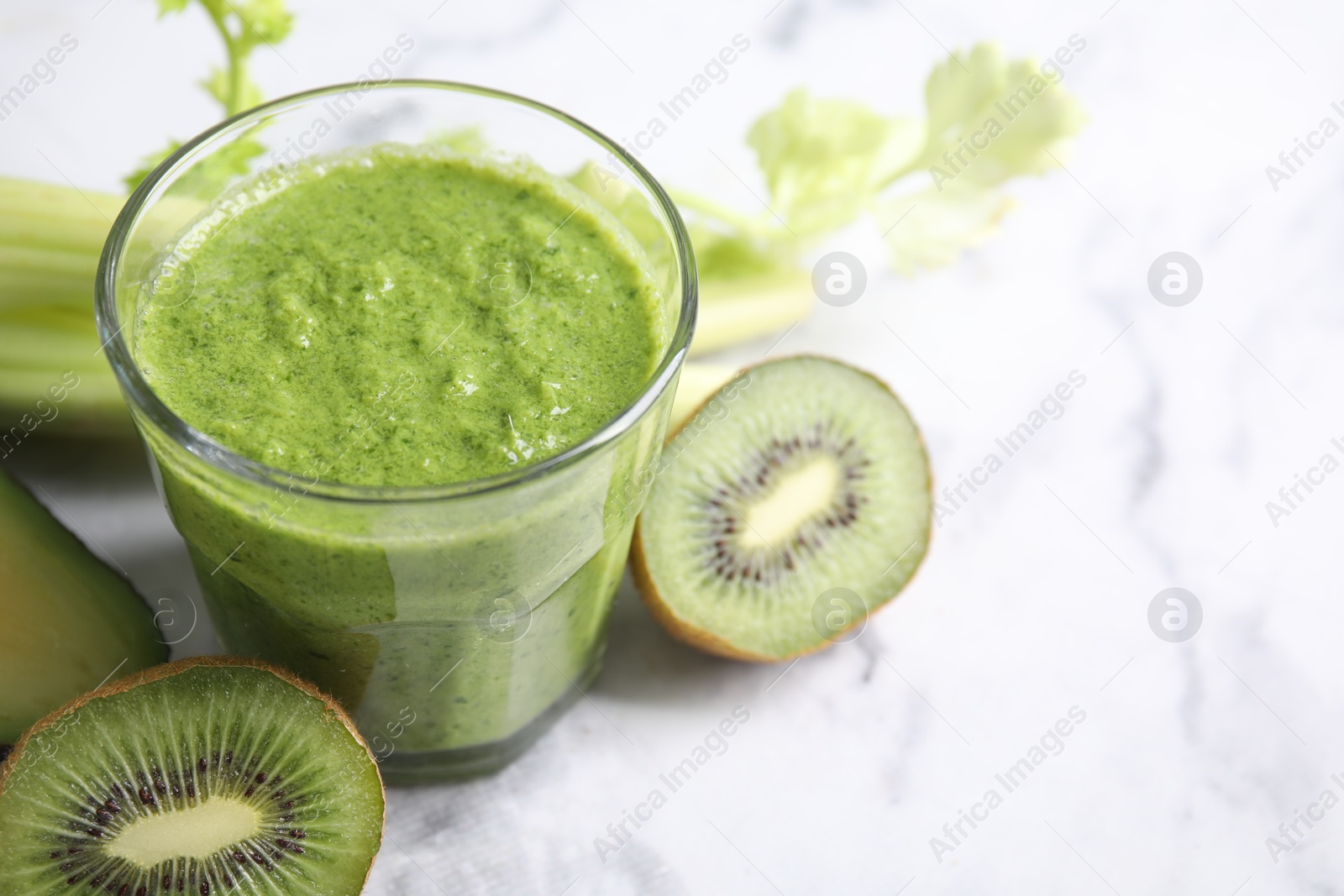 Photo of Delicious green smoothie and ingredients on white marble table, closeup. Space for text