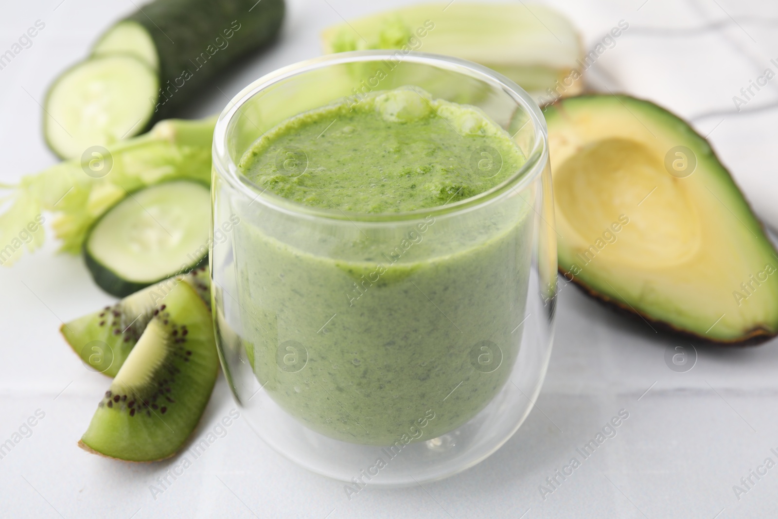 Photo of Delicious green smoothie and ingredients on white table, closeup