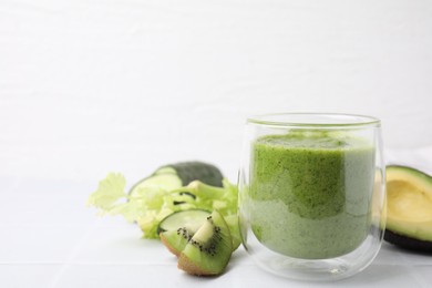 Photo of Delicious green smoothie and ingredients on white table. Space for text