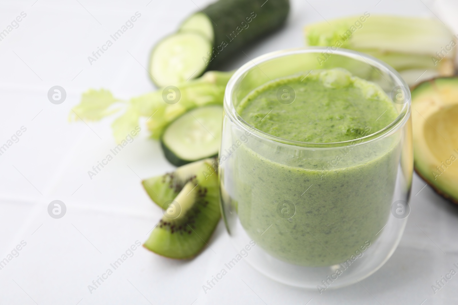 Photo of Delicious green smoothie and ingredients on white table, closeup. Space for text