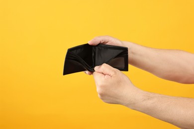 Photo of Man with empty wallet on yellow background, closeup. Space for text