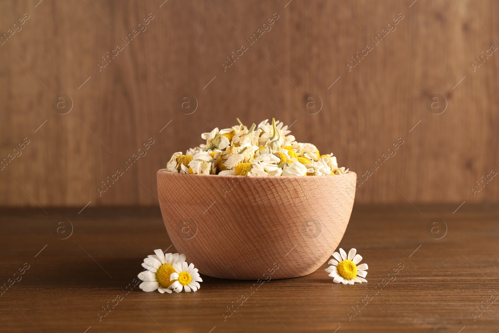 Photo of Dry and fresh chamomile flowers in bowl on wooden table